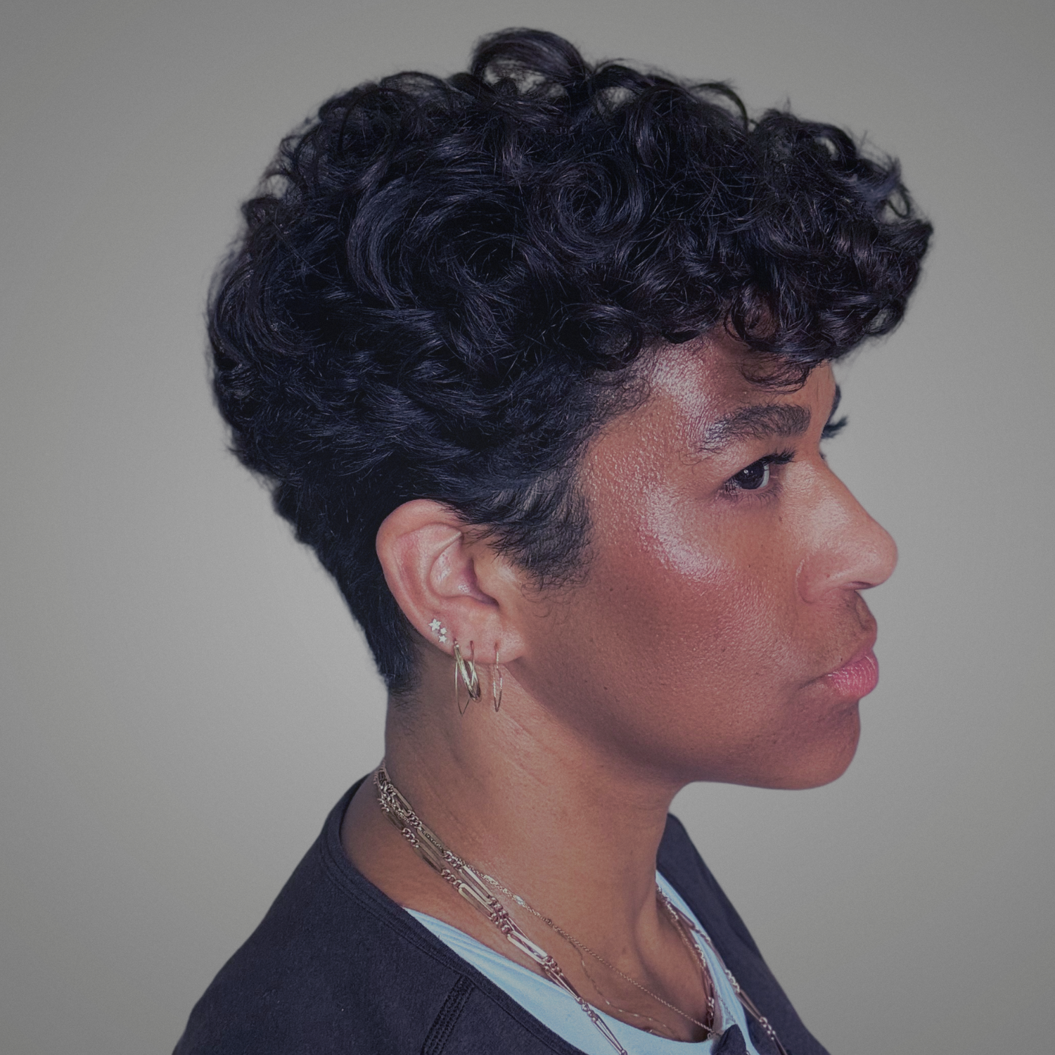 Side profile of Mandy Bynum with short curly hair against a neutral background